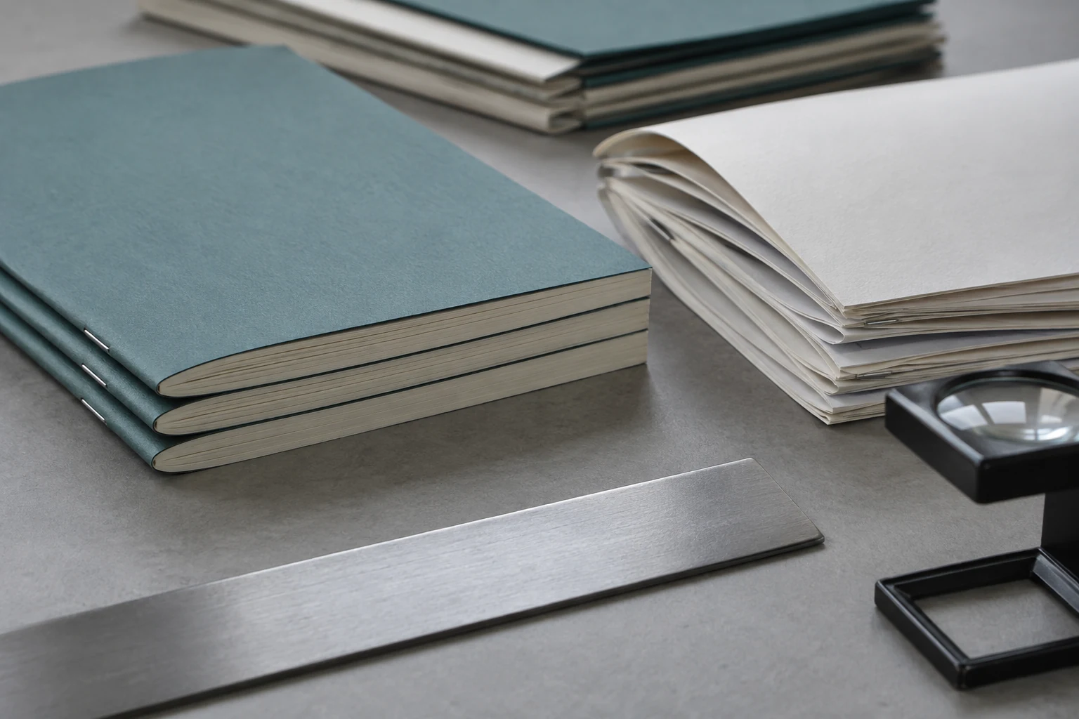 Teal stitched booklets and ivory folded paper samples beside a ruler and printer loupe