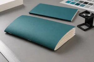 Saddle stitch creep review with a teal folded booklet, exposed nested paper edges and a printer loupe